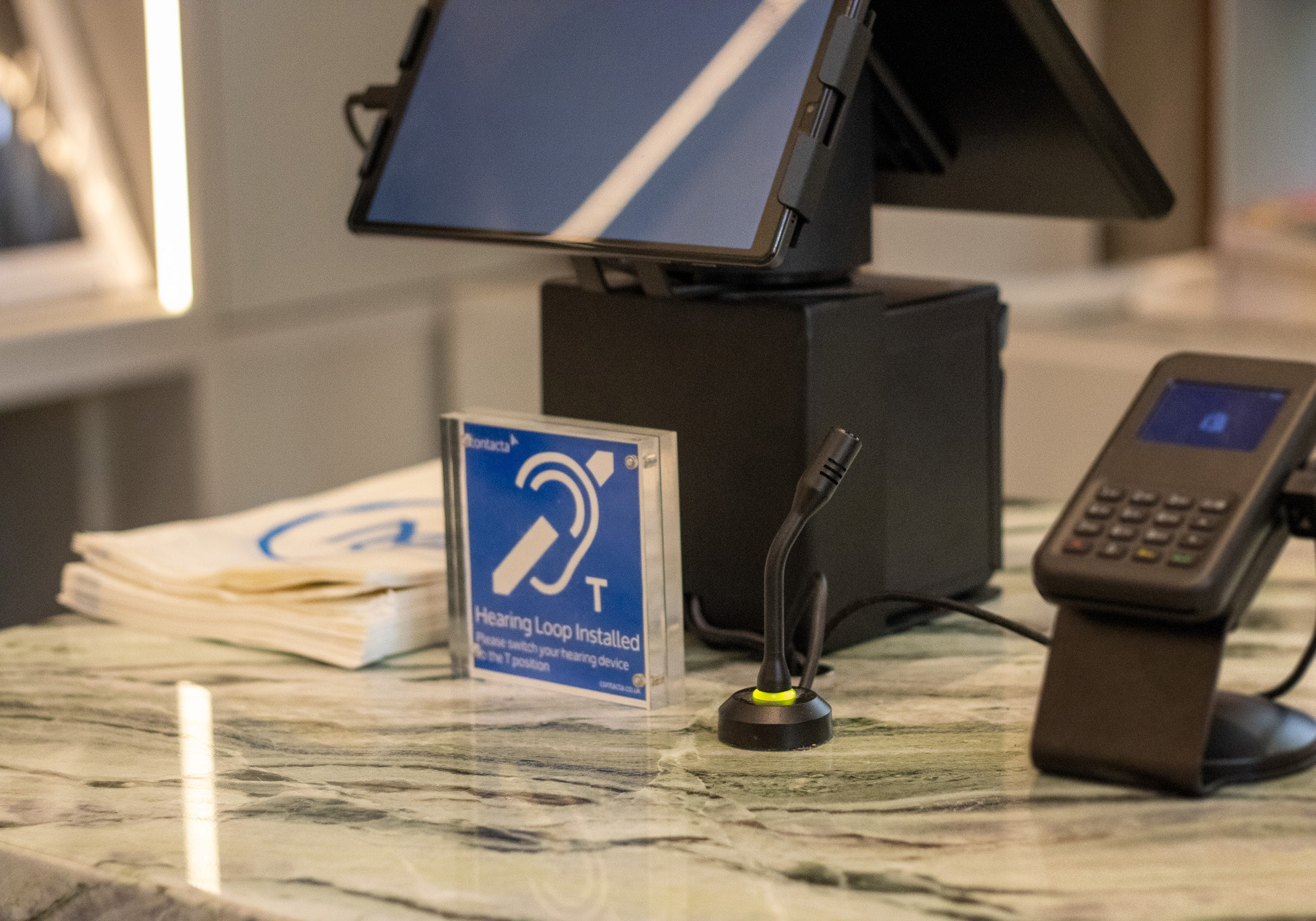 Close up of hearing loop sign on shop counter with chip & pin machine and small mounted microphone